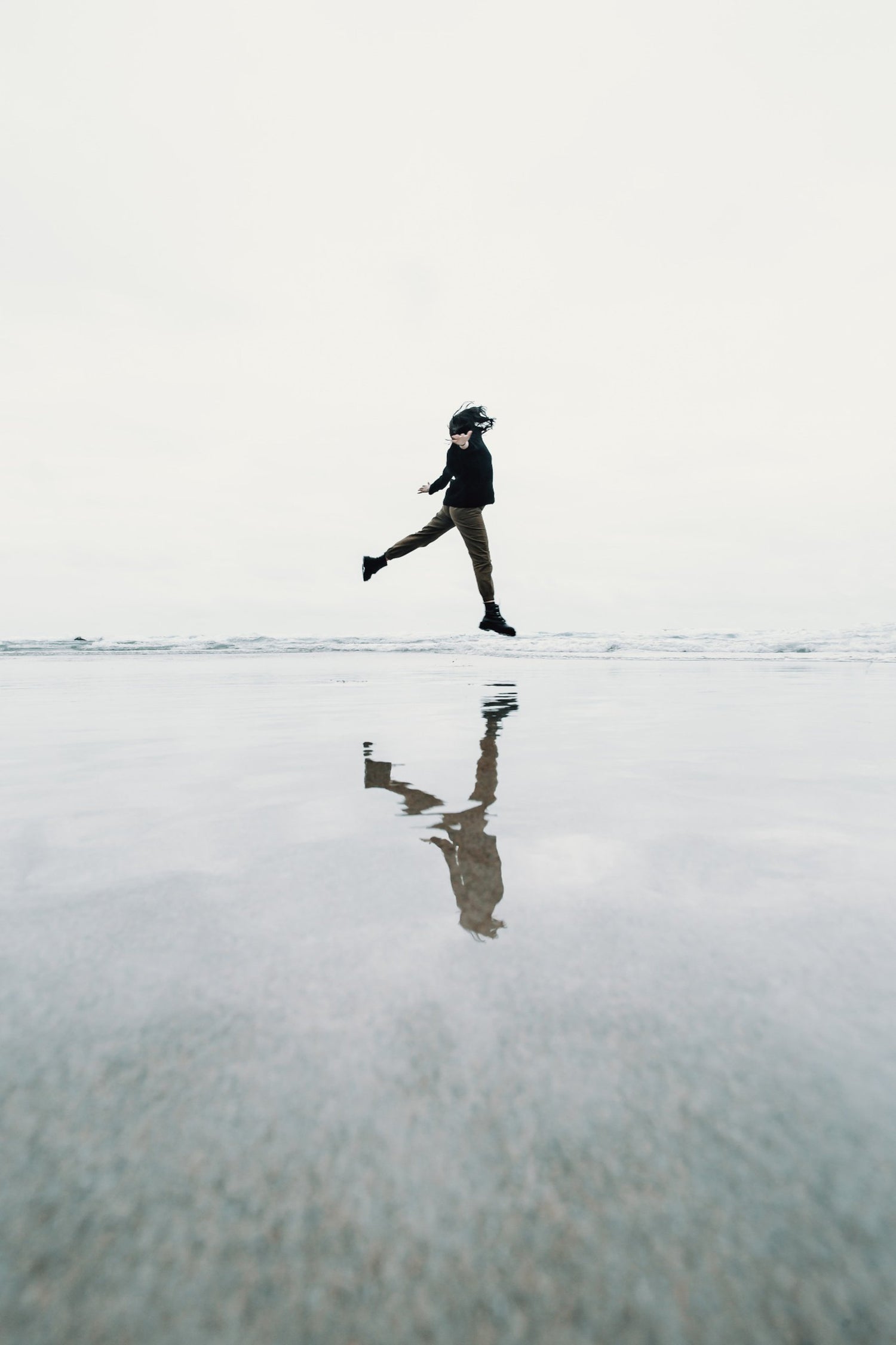 Person scheint über dem Wasser am Strand zu schweben, eine optische Illusion, die Leichtigkeit und Freiheit symbolisiert, inspiriert von der natürlichen Kraft und Balance der Vitalpilze.